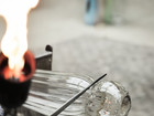 Glassblower heating and shaping molten glass with a flame.