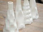 Four white ceramic vessels with textured surfaces on a wooden table.