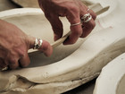 Hands shaping a clay bowl in a workshop.