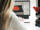 Person using a laptop with a 3D model next to a 3D printer.