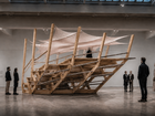 Large timber structure with stairs and stretched fabric in an exhibition hall with visitors.