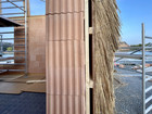 Close-up of a wall under construction with red clay blocks, timber framing and bundles of reeds.