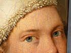Detail of a cracked painting showing two blue-grey eyes and a ruler along the right edge.