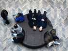 People sitting and lying on a circular bench surrounded by herringbone-patterned flooring.