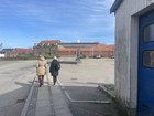 Two people walking along a pavement towards a petrol station and red brick buildings.