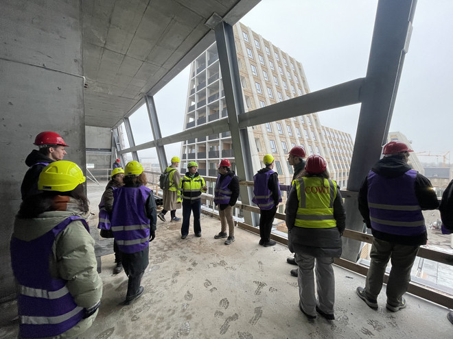 Rygvendte personer iført sikkerhedshjelme besøger en byggeplads