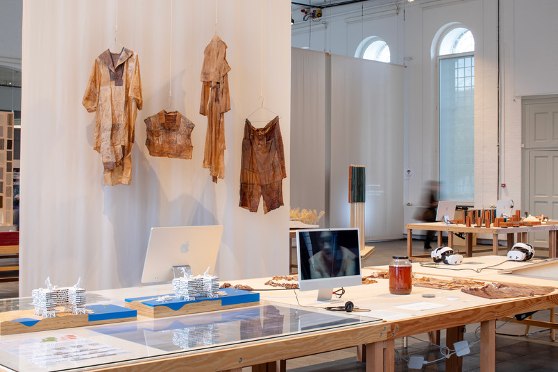 Table with design models, a computer, and hanging garments.