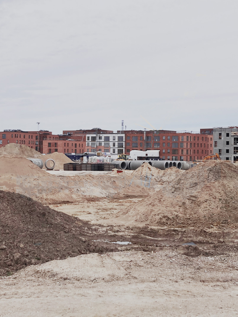 Construction site with soil piles and large concrete pipes in front of new residential buildings.