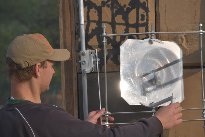 Person adjusting a transparent lens in a metal frame in front of a wall.