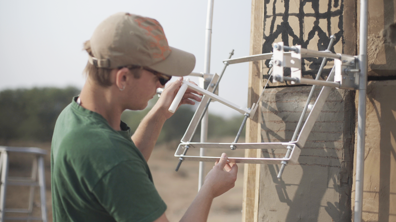 Person adjusting a metal frame with mounted lenses on a wall.