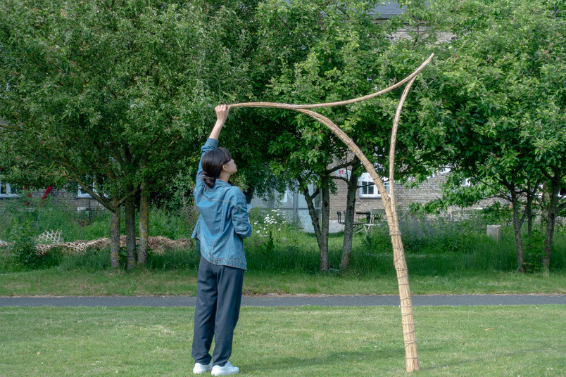 Person adjusting a curved bamboo structure on a lawn.