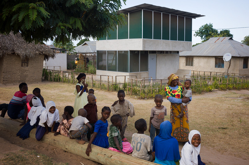 Children and adults gathered in front of a building in a village setting.