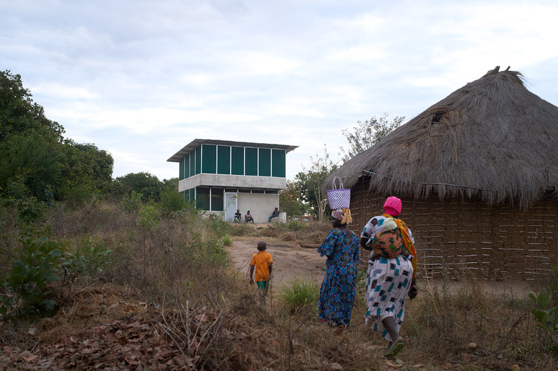People walking along a path between traditional houses and a modern two-storey building.