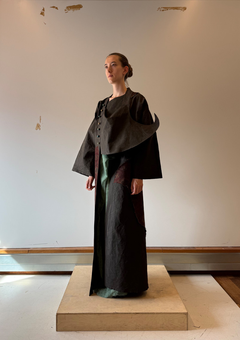 Model wearing a dark layered garment inspired by a moving temple, with an extended eave-like structure and faded textile surfaces suggesting incense smoke, time, wind, and rain.