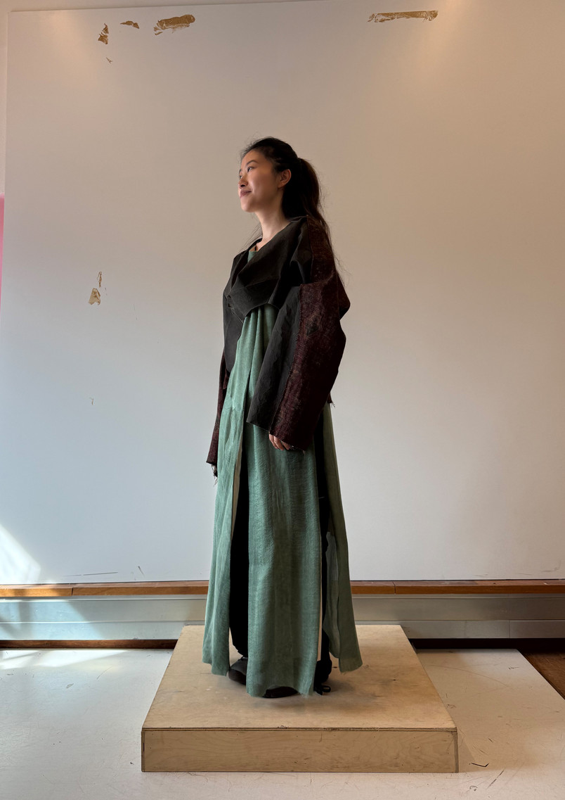 Model wearing a green garment developed by transforming flat temple-derived pattern structures into a three-dimensional form through the drifting movement of incense smoke.