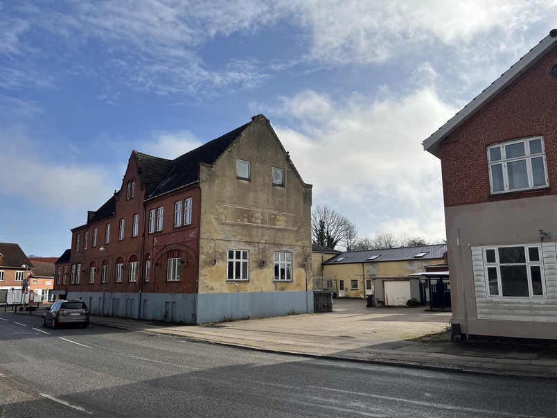 Street corner with an older red brick and yellow plaster building, a parked car, and low-rise buildings around
