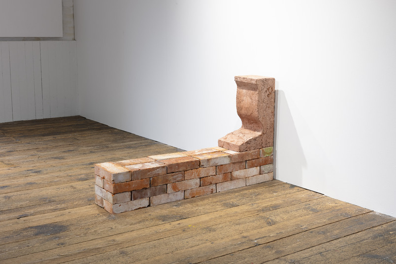 Brick installation with a small built form along a wall on a wooden floor