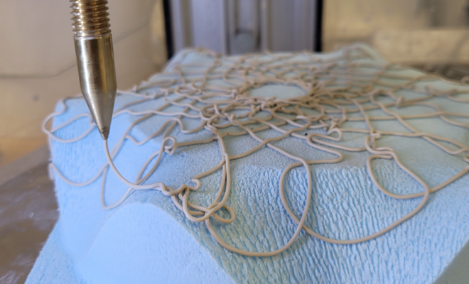 Close-up of a 3D printer extruding clay onto a curved surface.