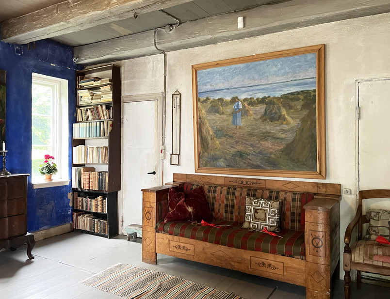 Photo of historical interior with sofa, painting, and book shelf.