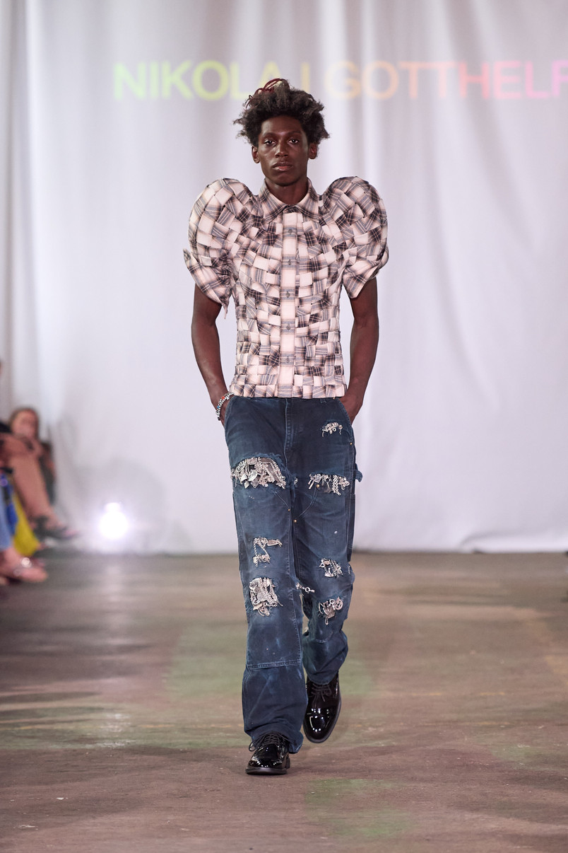 Model on a runway wearing a checked top with dramatic puff sleeves and distressed dark blue jeans.