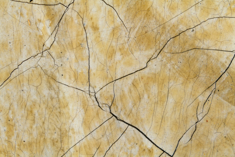 Close-up of a yellowed, crackled paint surface with fine and broad dark cracks