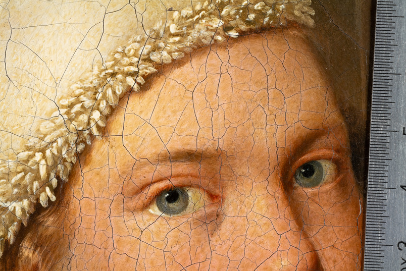 Detail of the eyes and forehead in an old painted portrait, showing pronounced craquelure and a measurement scale.