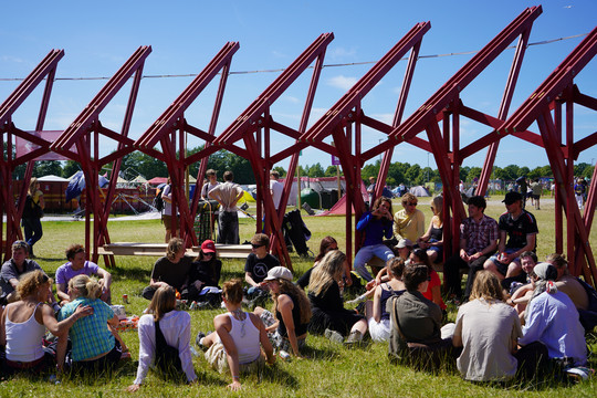 Red support beams in the background, young people sitting on the grass in the foreground