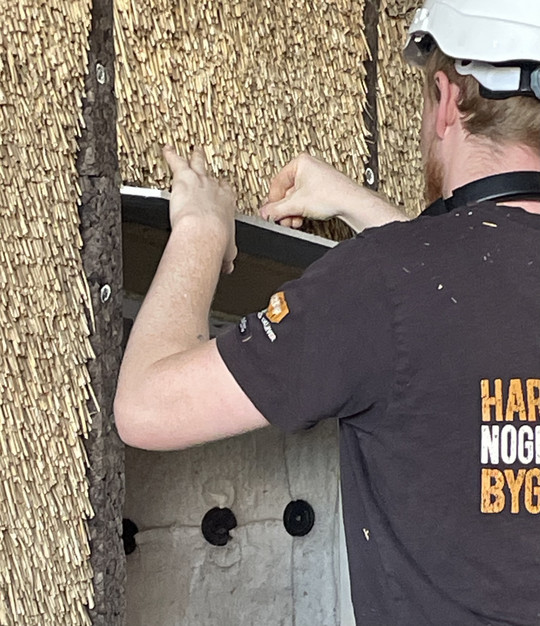 Rear-facing figure positioning reed thatch on a vertical façade surface