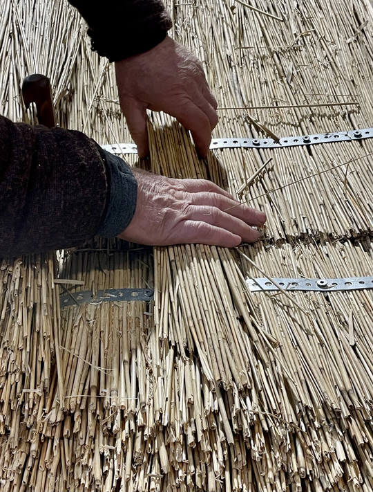 Hands thatching a roof.