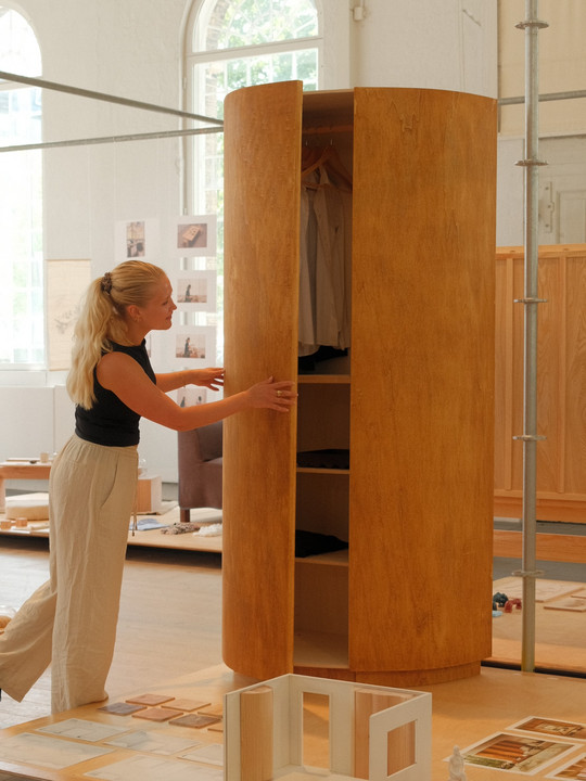 Person opening a round wooden wardrobe with shelves and clothes.