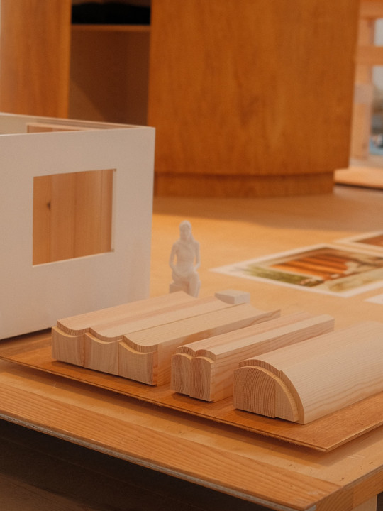 Wooden models and miniature figure on table next to architectural model.