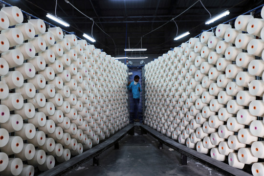 Rows of large white cotton spools in a textile factory under artificial lighting.