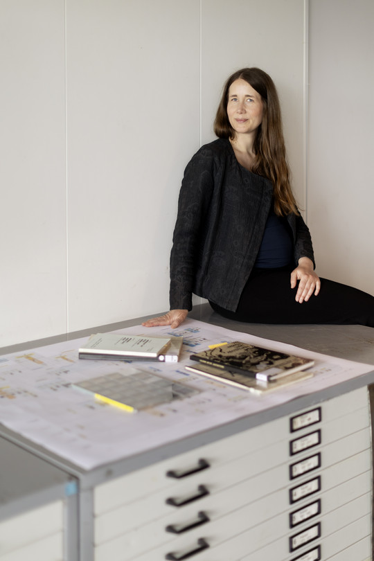 Color photograph of Christine Bjerke sitting on a archive furniture with archival materials next to her. 
