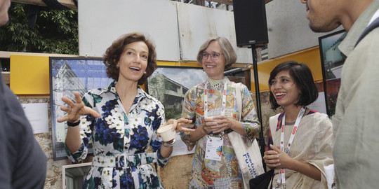  Three people conversing at an exhibition with architectural images.