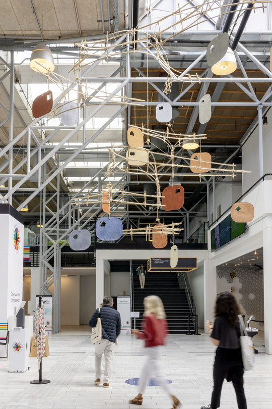 Atrium with suspended art installation and visitors in motion.