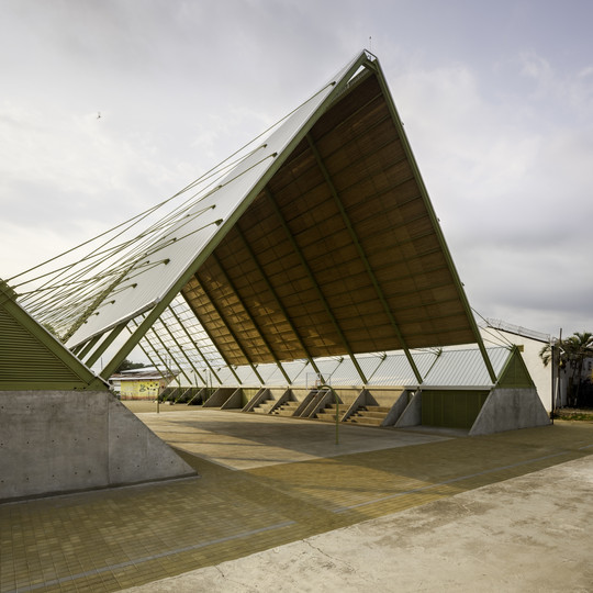 Open pavilion with a tall sloped roof covering an outdoor court.