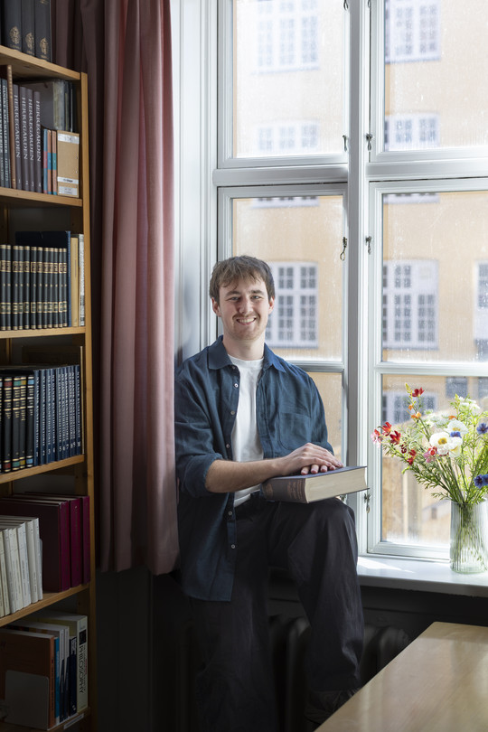 James sitting by the window in a library, with a book in his hands.