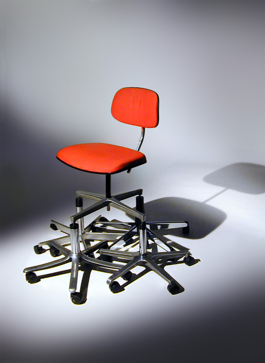 Red office chair stands atop a pile of wheeled chair bases.