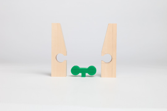 Two separated wooden parts with a green connector placed between them.
