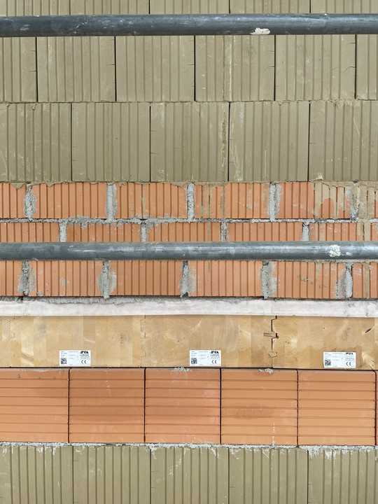 Detail of brickwork with green and red bricks, a horizontal wooden beam, and scaffolding pipes.