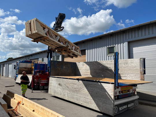 A lorry-mounted crane lifts a large timber structure above the bed of a lorry.