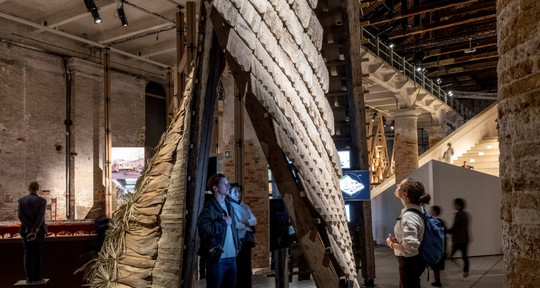 Visitors examine a tall, inclined structure with textured panels at an exhibition.