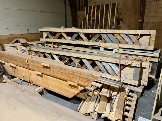 Large timber lattice structures and beams are stacked and secured with straps in a workshop.