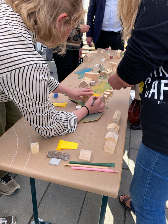 Citizens work together on an urban model featuring small wooden houses, green spaces and coloured notes.
