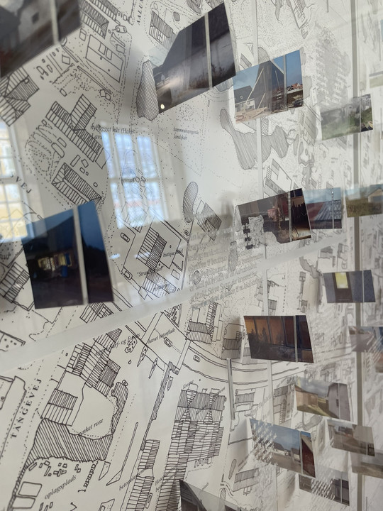 Exhibition featuring photographs of buildings and urban spaces mounted in front of a detailed, hand-drawn city map.