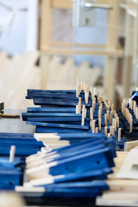 Blue-painted wooden pieces with small wooden pegs stacked on a worktable.