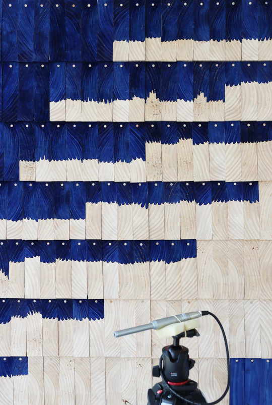 Close-up of wooden panels with wavy blue patterns and a microphone on a stand in front.
