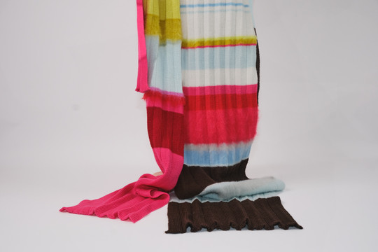 Colorful knitted textile in pink, red, light blue, yellow and brown with stripes and varied textures.