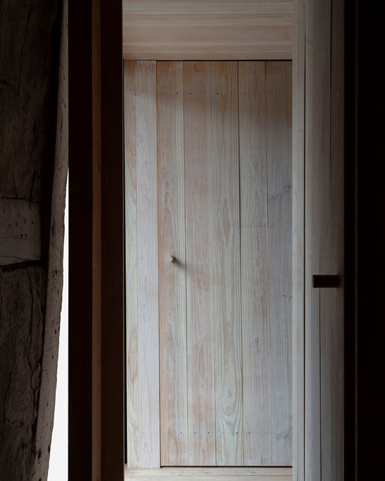 Light timber door made of vertical planks, framed by dark timber beams.