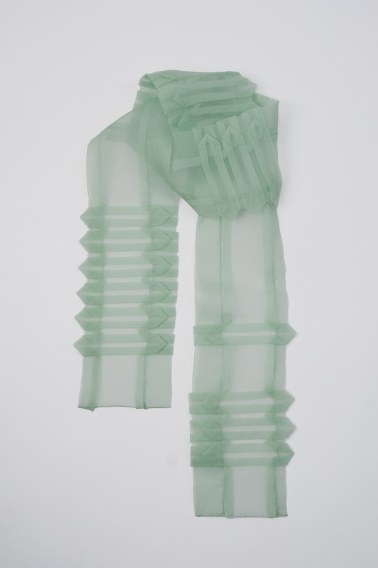Sheer mint-green scarf with geometric pleats and folded details against a white background